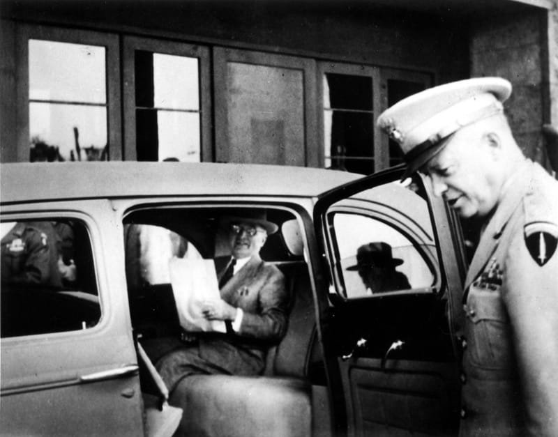 Truman reading a newspaper with Eisenhower at the door of his car