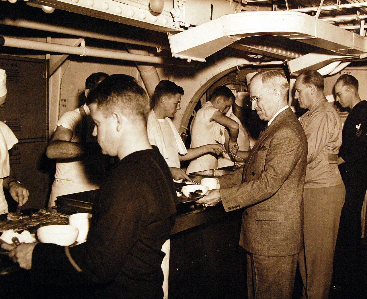 80-G-49928: Potsdam Conference, 17 July – 2 August 1945. President Harry S. Truman onboard USS Augusta (CA 31) en-route to Antwerp for the “Big Three” Conference. Shown: Being served in crew’s mess hall. Faces which can be seen in the picture are: (left to right): S1/C Albert Rice; S1/c J.W. Leinback; S1/C .W. Smith, the President, a secret service man and PhM2/C Elmo C. Buck. Photograph received July 18, 1945. U.S. Navy Photograph, now in the collections of the National Archives. (2016/02/23).