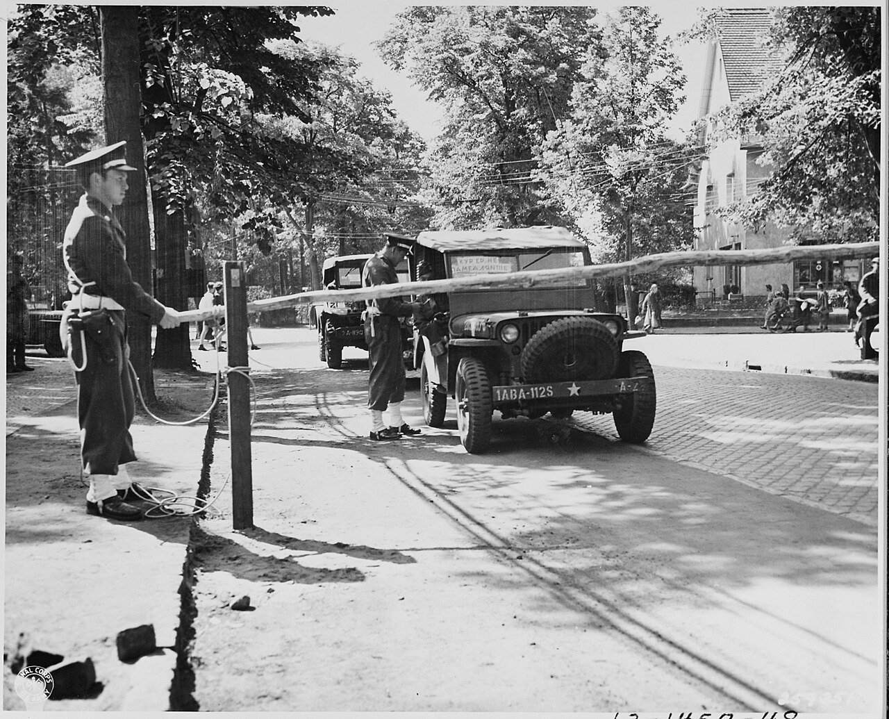 Military Police of the 713th MP Bn., check vehicles and personnel at a road barrier in the American compound of the…