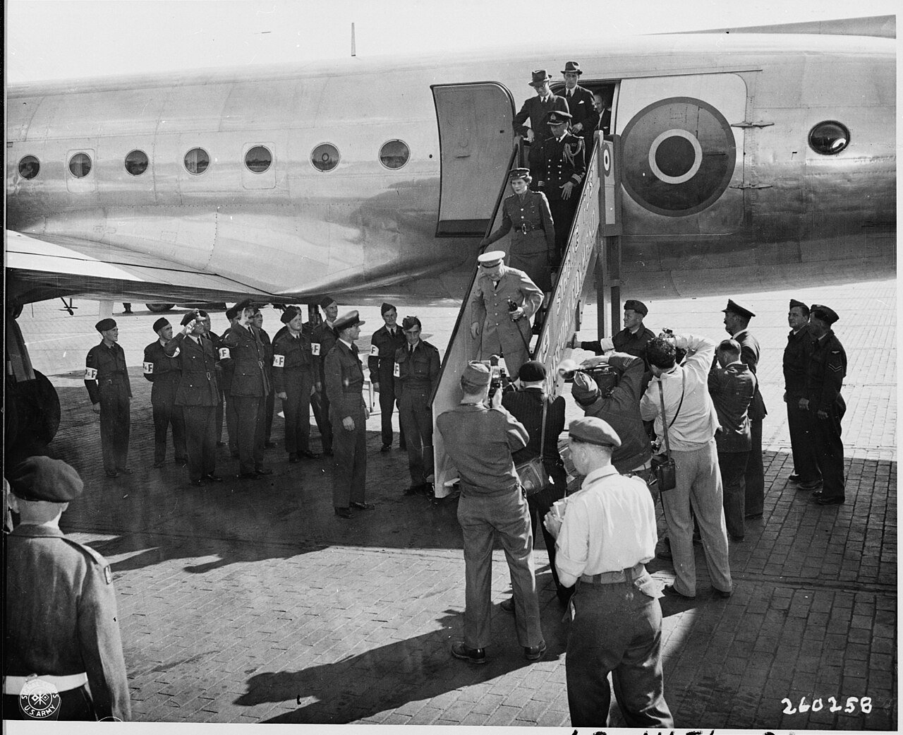 Prime Minister Winston Churchill, surrounded by cameramen and dignitaries, leaves the airplane which brought him to…